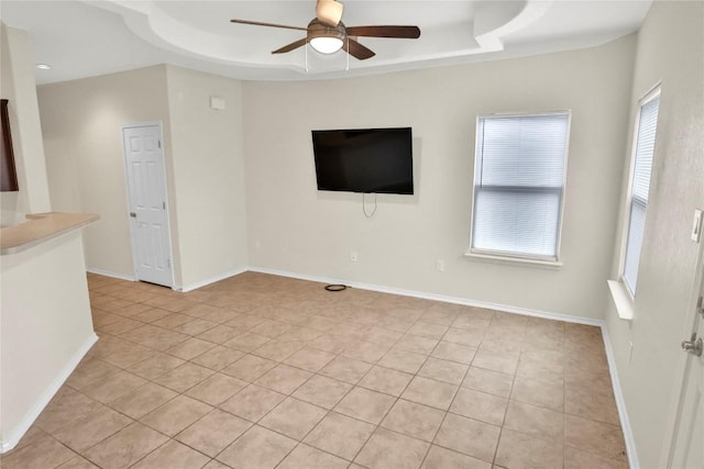 interior space with a ceiling fan, a tray ceiling, and baseboards