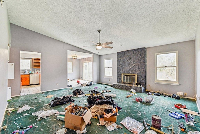 unfurnished living room featuring baseboards, lofted ceiling, ceiling fan, a textured ceiling, and a stone fireplace