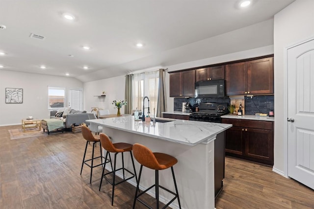 kitchen with a center island with sink, visible vents, a breakfast bar area, open floor plan, and black appliances