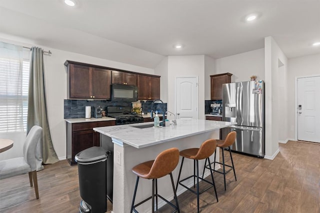 kitchen featuring a center island with sink, decorative backsplash, dark wood finished floors, dark brown cabinets, and black appliances