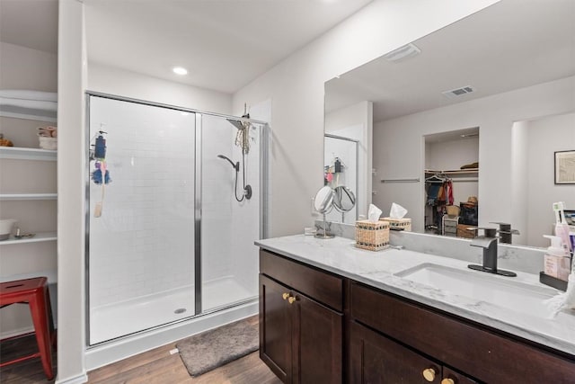 bathroom with visible vents, wood finished floors, a spacious closet, vanity, and a shower stall