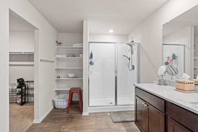 bathroom with wood finished floors, vanity, baseboards, a spacious closet, and a stall shower