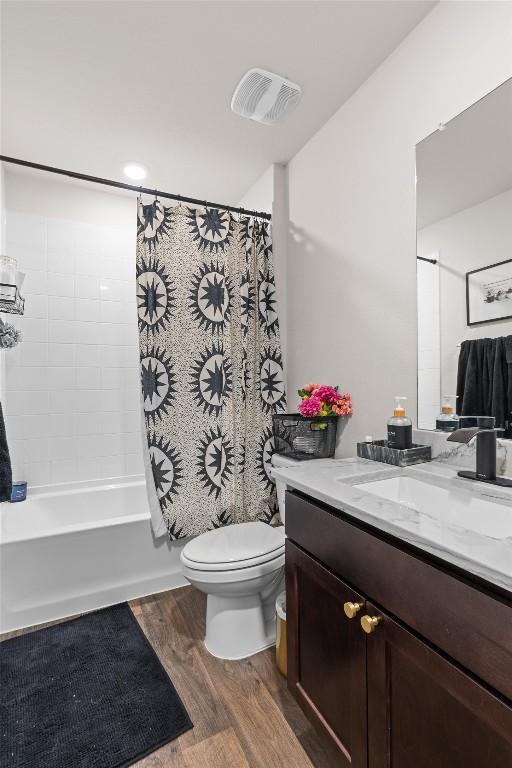 full bathroom with visible vents, toilet, wood finished floors, shower / bath combo with shower curtain, and vanity