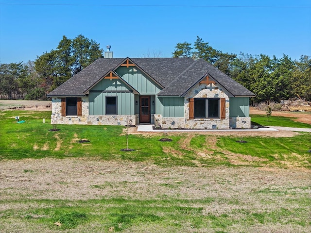 view of front facade with stone siding, a front yard, board and batten siding, and roof with shingles