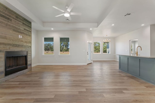 unfurnished living room with light wood-style floors, a raised ceiling, visible vents, and a large fireplace