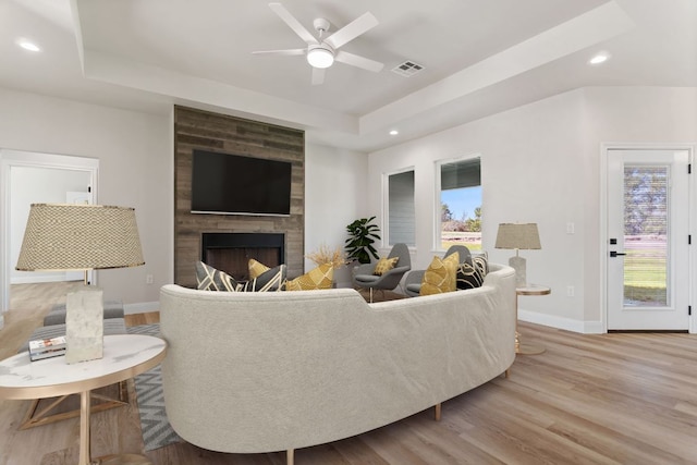 living room featuring a large fireplace, baseboards, visible vents, a tray ceiling, and light wood-style floors