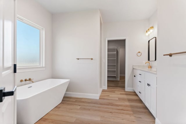 full bathroom featuring baseboards, wood finished floors, a walk in closet, vanity, and a freestanding tub