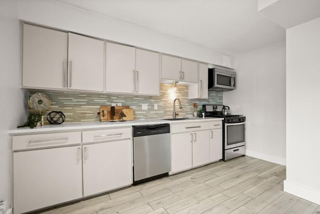 kitchen featuring stainless steel appliances, light countertops, decorative backsplash, white cabinetry, and a sink