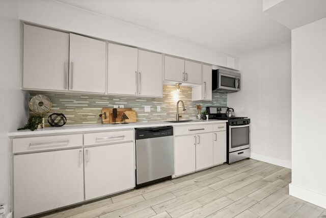 620 S 1st St Unit 104, Austin, TX 78704 - kitchen featuring stainless steel appliances, light countertops, backsplash, light wood finished floors, and white cabinetry