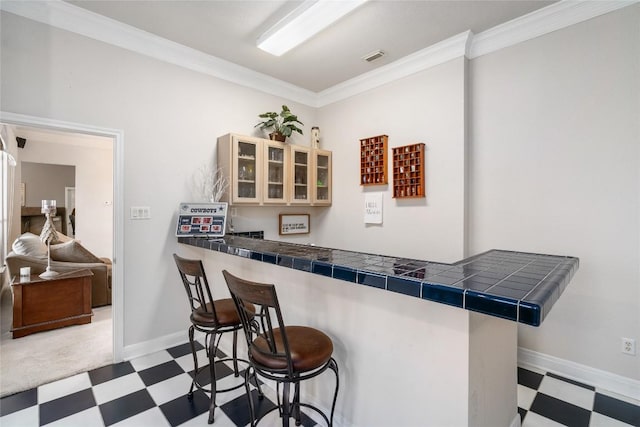 kitchen featuring tile counters, glass insert cabinets, a kitchen breakfast bar, crown molding, and light floors