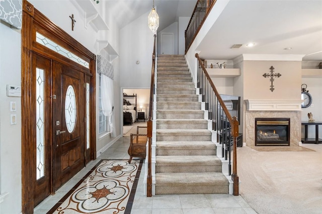 foyer featuring visible vents, a high ceiling, stairs, crown molding, and a high end fireplace