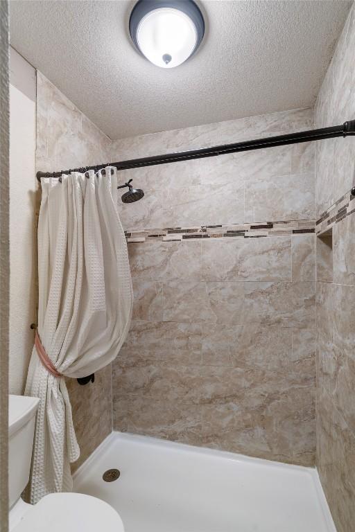 bathroom with a textured ceiling, a tile shower, and toilet