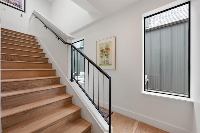 stairs featuring baseboards, a wealth of natural light, and wood finished floors