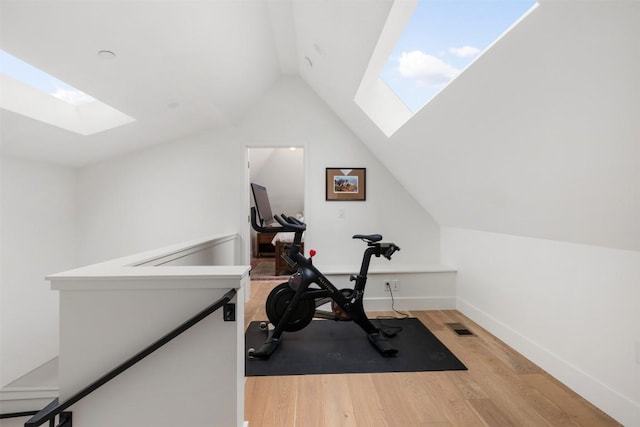 workout area with lofted ceiling with skylight, light wood-style flooring, visible vents, and baseboards