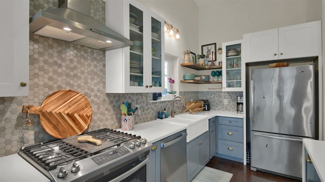 kitchen with wall chimney range hood, white cabinetry, glass insert cabinets, and stainless steel appliances