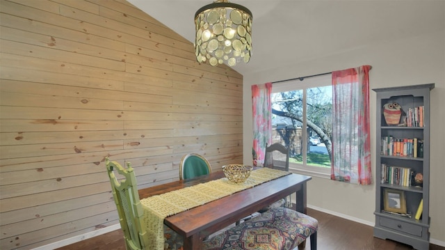 dining space featuring lofted ceiling, wooden walls, a notable chandelier, baseboards, and dark wood-style floors