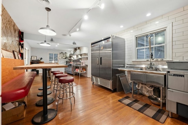 kitchen with stainless steel countertops, built in refrigerator, decorative light fixtures, and light wood-style floors