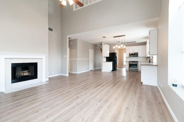 8507 Chat Ln, Round Rock, TX 78681 - unfurnished living room with a fireplace, light wood-style floors, a ceiling fan, and a towering ceiling