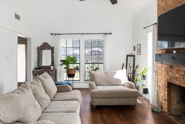 living room with visible vents, ceiling fan, dark wood-style flooring, a brick fireplace, and high vaulted ceiling