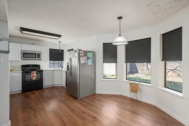 kitchen with dark wood finished floors, light countertops, hanging light fixtures, appliances with stainless steel finishes, and white cabinets