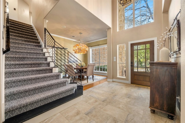 entryway featuring baseboards, ornamental molding, an inviting chandelier, a high ceiling, and stairs