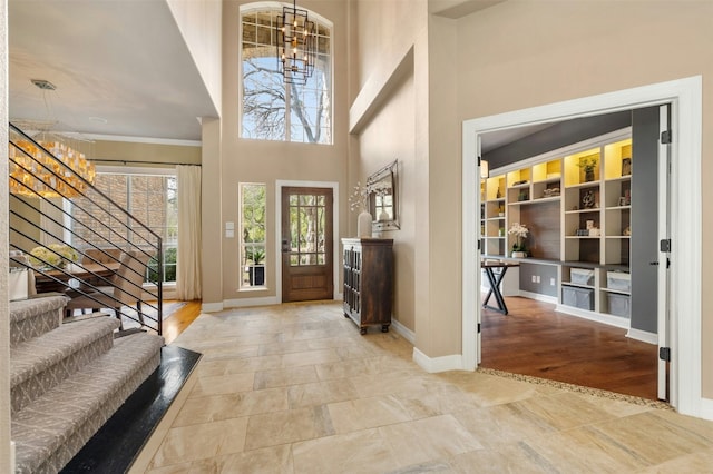 foyer entrance with a high ceiling, an inviting chandelier, stairs, and baseboards