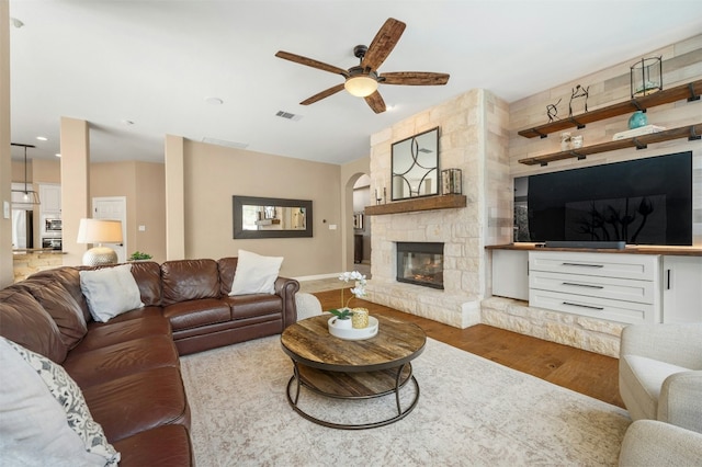 living area with ceiling fan, a fireplace, wood finished floors, visible vents, and baseboards