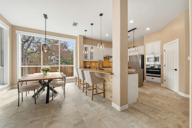 kitchen with glass insert cabinets, light stone countertops, stainless steel appliances, white cabinetry, and pendant lighting