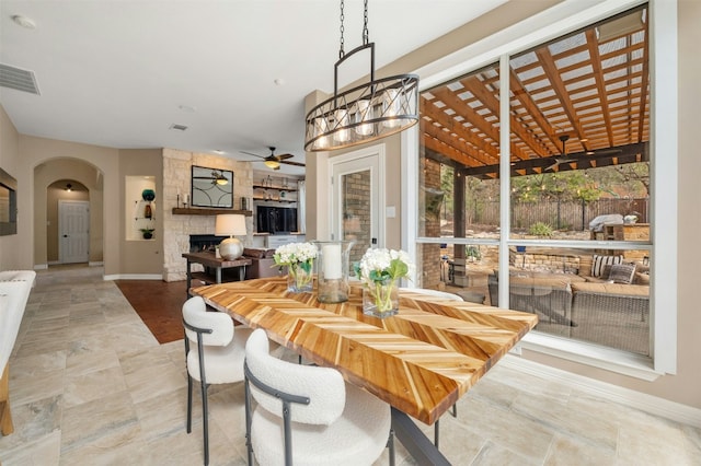 dining space featuring arched walkways, a fireplace, visible vents, ceiling fan, and baseboards