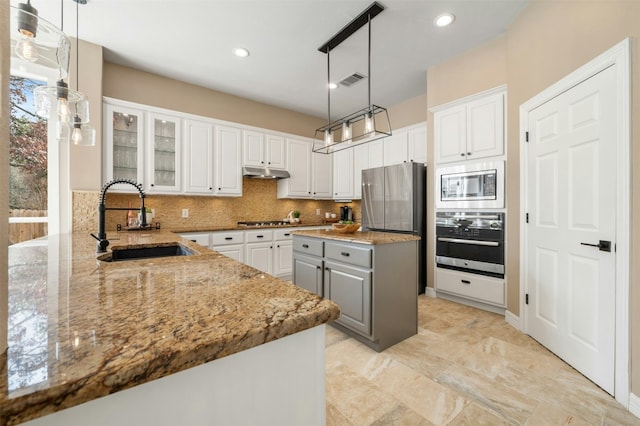 kitchen with pendant lighting, stainless steel appliances, glass insert cabinets, white cabinets, and a sink