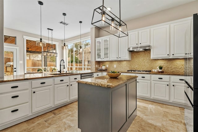 kitchen featuring hanging light fixtures, a kitchen island, light stone countertops, and white cabinets