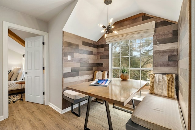 dining space featuring light wood finished floors, an inviting chandelier, an accent wall, vaulted ceiling, and wooden walls