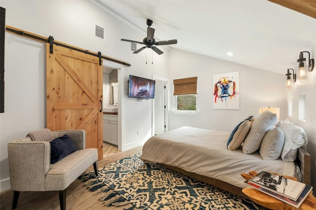 bedroom with light wood finished floors, visible vents, ensuite bathroom, a barn door, and vaulted ceiling