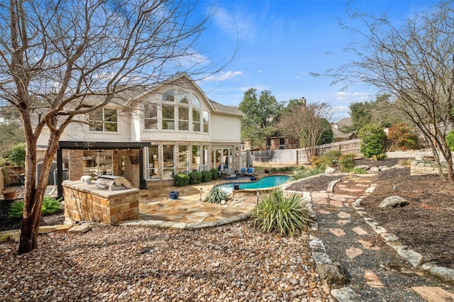 back of house with a fenced in pool, a patio area, fence, and an outdoor kitchen