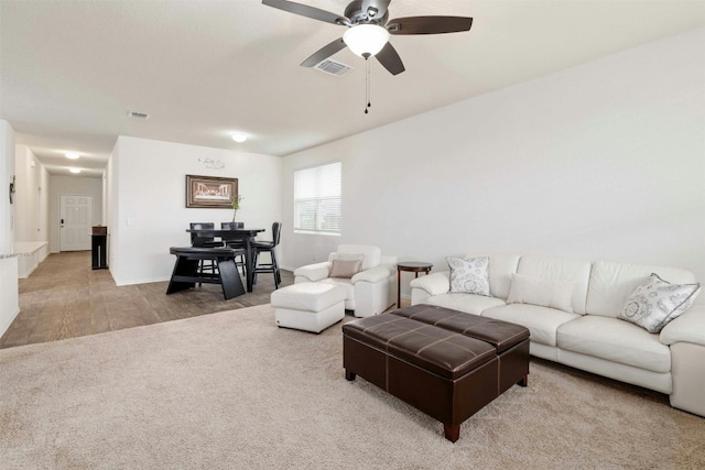 living room featuring light carpet, light wood finished floors, ceiling fan, and visible vents