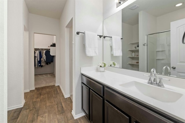 full bathroom featuring baseboards, wood finished floors, a walk in closet, vanity, and a shower stall