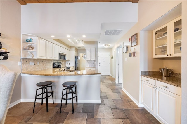 kitchen featuring a breakfast bar, appliances with stainless steel finishes, glass insert cabinets, white cabinets, and a peninsula