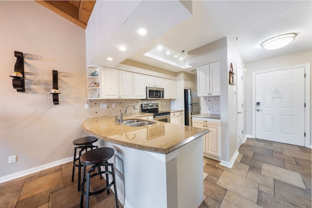 kitchen featuring appliances with stainless steel finishes, white cabinetry, a sink, and a peninsula