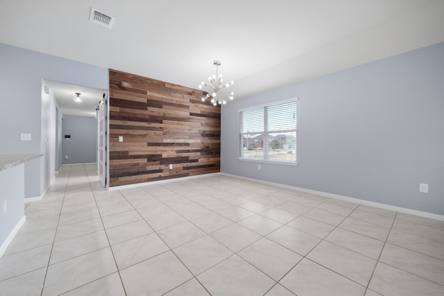 spare room with a chandelier, wooden walls, an accent wall, visible vents, and baseboards