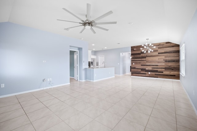 unfurnished living room with baseboards, lofted ceiling, an accent wall, wood walls, and ceiling fan with notable chandelier