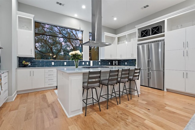 4907 Timberline Dr, Austin, TX 78746 - kitchen featuring appliances with stainless steel finishes, island exhaust hood, light wood-type flooring, a kitchen island, and decorative backsplash