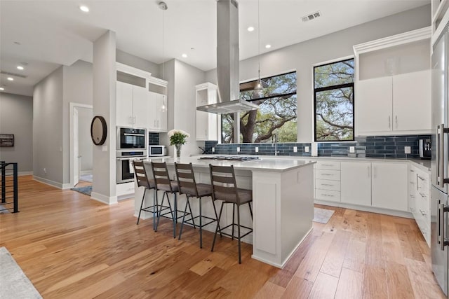4907 Timberline Dr, Austin, TX 78746 - kitchen with island exhaust hood, decorative backsplash, a center island, light wood finished floors, and recessed lighting