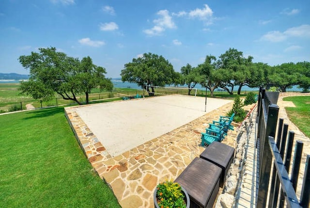 view of property's community with volleyball court, a lawn, a water view, and fence