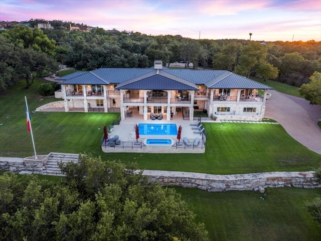 back of property at dusk featuring a balcony, metal roof, stairs, a yard, and a patio area