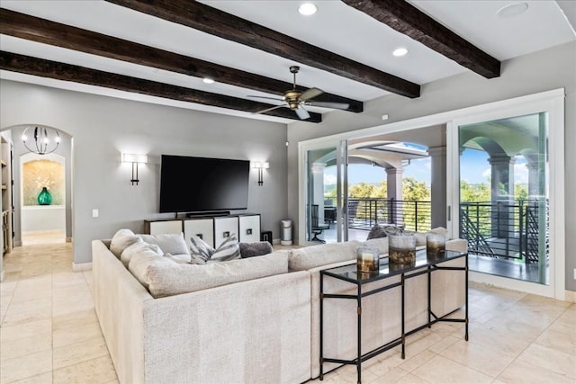 living room featuring arched walkways, light tile patterned floors, a ceiling fan, baseboards, and beamed ceiling