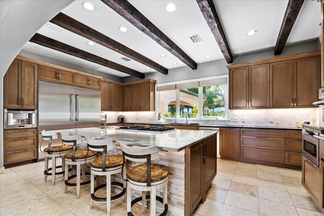 kitchen featuring brown cabinetry, stainless steel appliances, a kitchen island with sink, and a breakfast bar