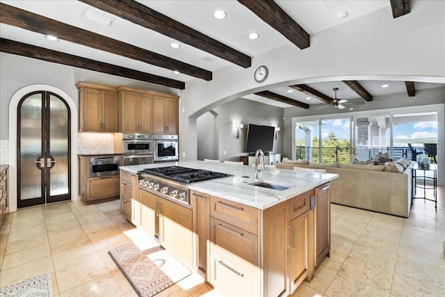 kitchen with arched walkways, appliances with stainless steel finishes, open floor plan, a sink, and an island with sink