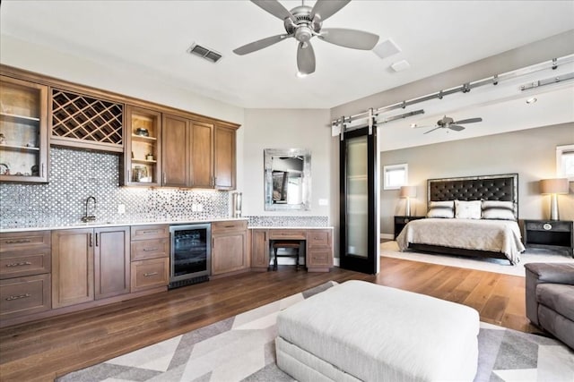 bedroom featuring wine cooler, a barn door, dark wood-style flooring, visible vents, and indoor wet bar