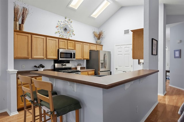 kitchen featuring light wood finished floors, appliances with stainless steel finishes, a kitchen bar, and visible vents