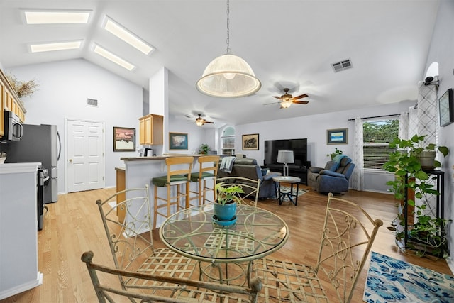 dining area with a skylight, light wood-style flooring, visible vents, and ceiling fan